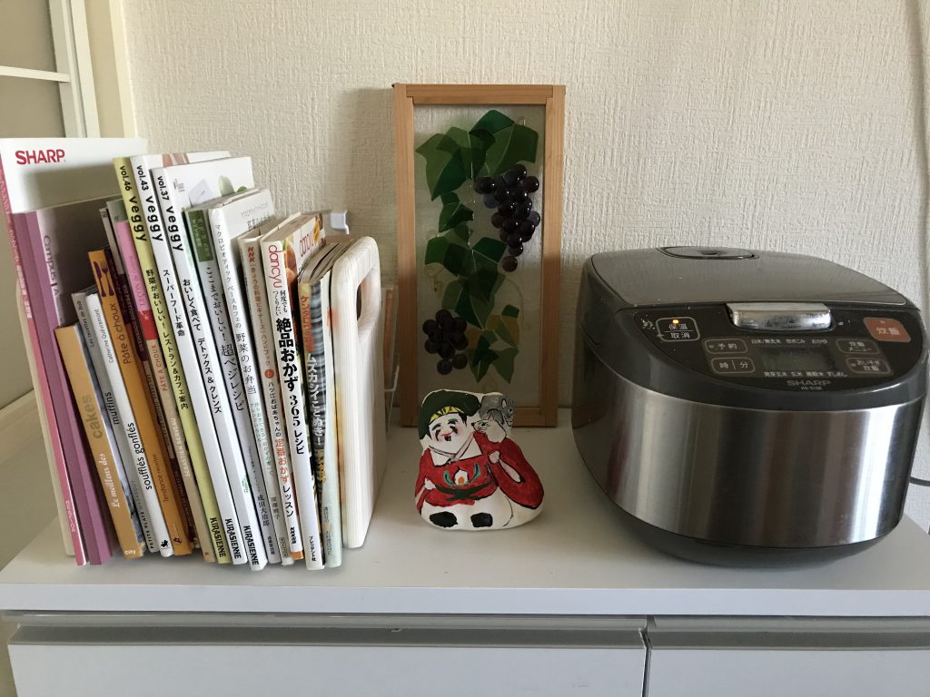 Daikokuten doll standing between recipe books and a rice cooker