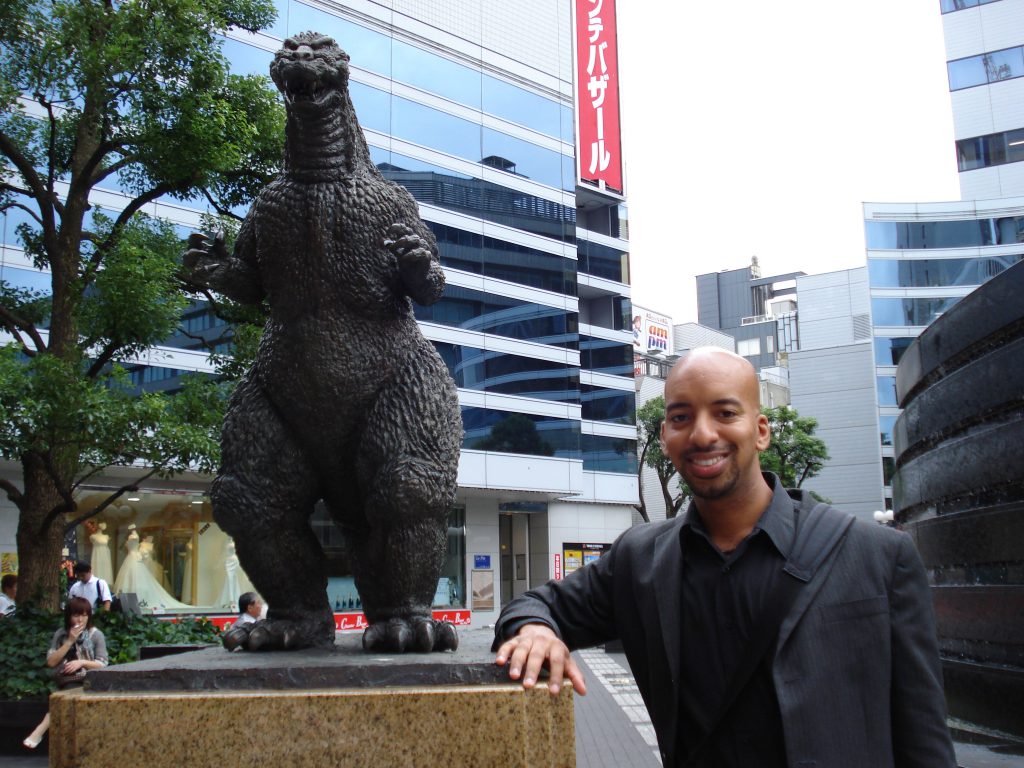 Anthony posing next to a small Godzilla statue