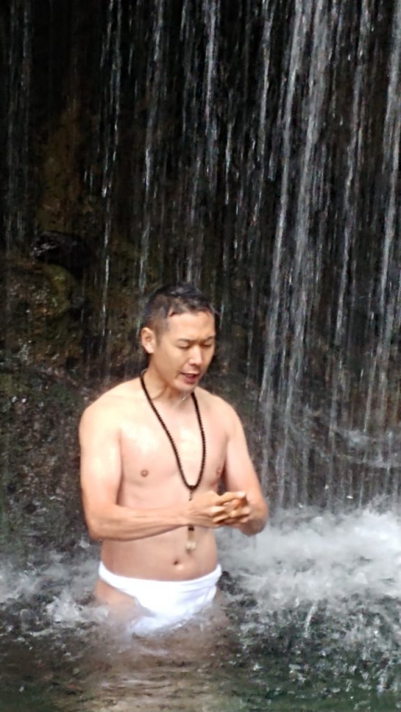 Mr. Tani practicing meditation, hands joined, under a waterfall