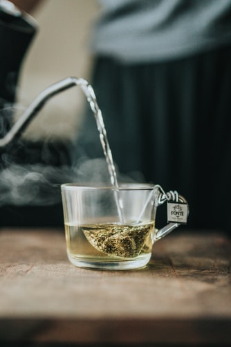 Hot water being poured directly on a  green teabag in a cup