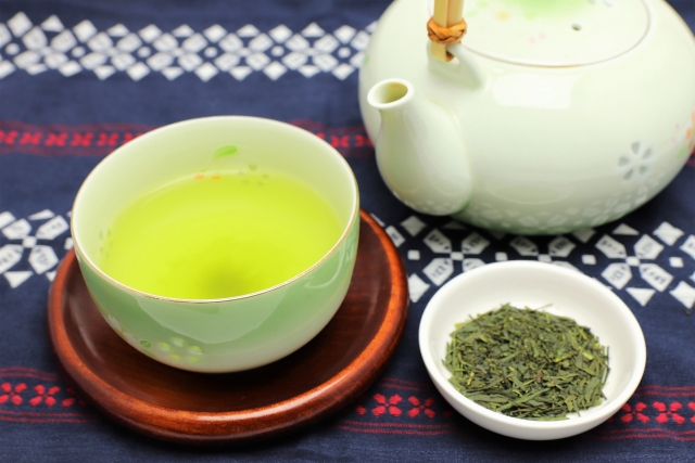 A pot, a cup of green tea and a small plate with green tea leaves