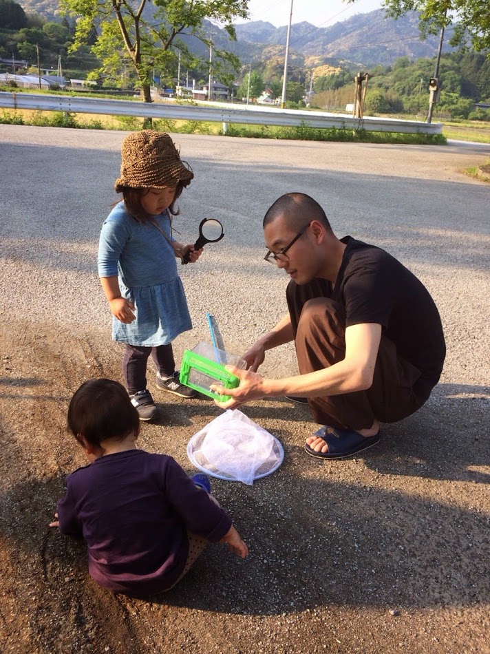 A man with a shaved head is playing at catching insects with two small children, a girl and a boy