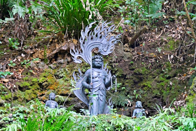 A fierce-looking bodhisattva statue. It is standing up, holds a sword, and is surrounded by flames