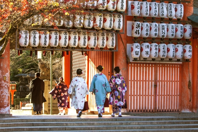 Four women and a man dressed in a kimono enter the gate of a Shinto shrine