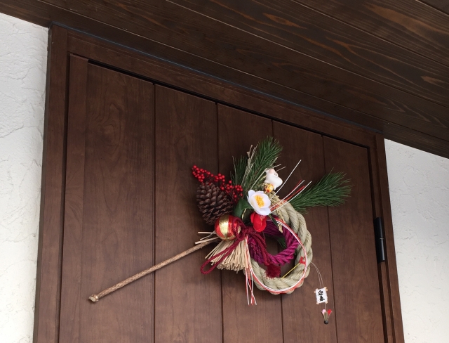 A Japanese traditional decoration made with a sacred cord, floers and pine is displayed on a door