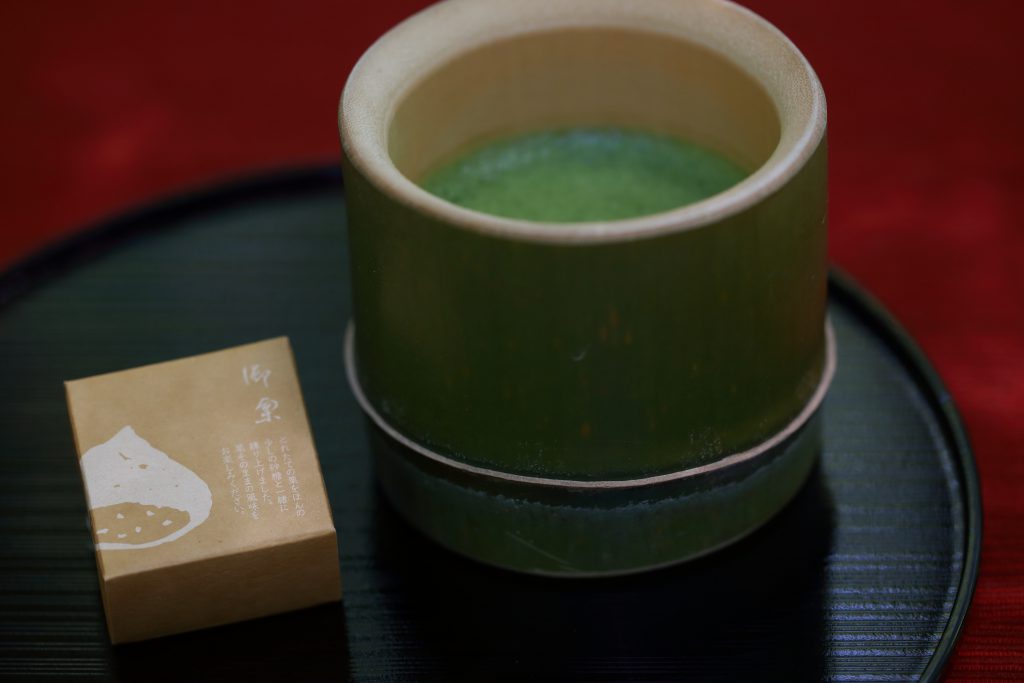 Green tea in a bamboo cup, and a sweet on a plate