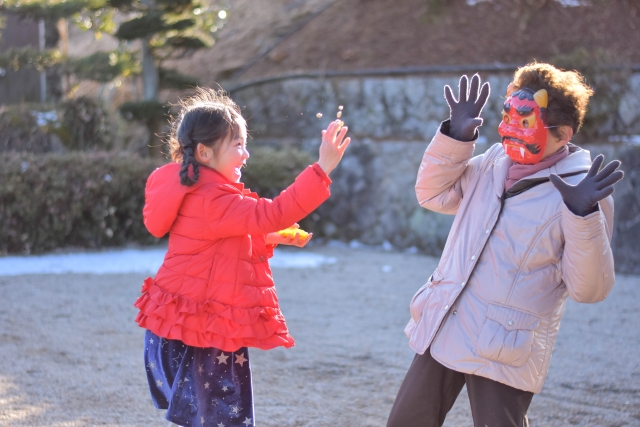 A little girl is throwing soybeans on  man disguised as a demon.