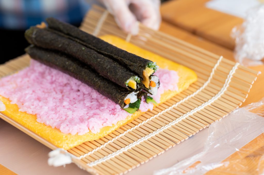 Several thin seaweed sushi rolls are about to be rolled in a bigger sushi