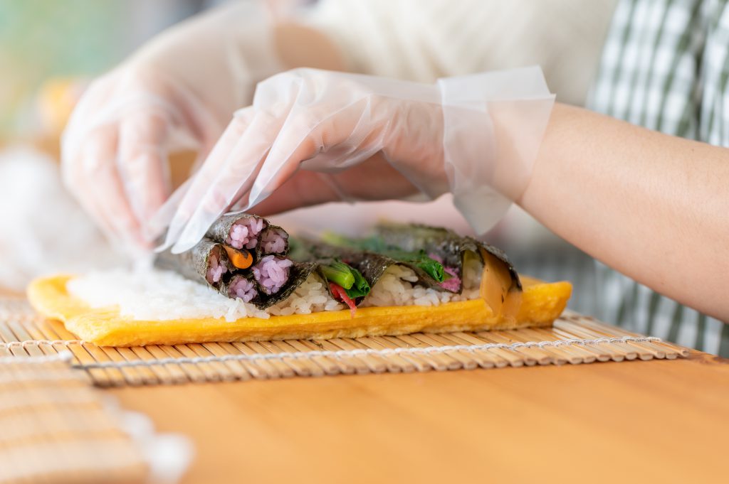 Two hands stacking several thin sushi rolls on top of each other