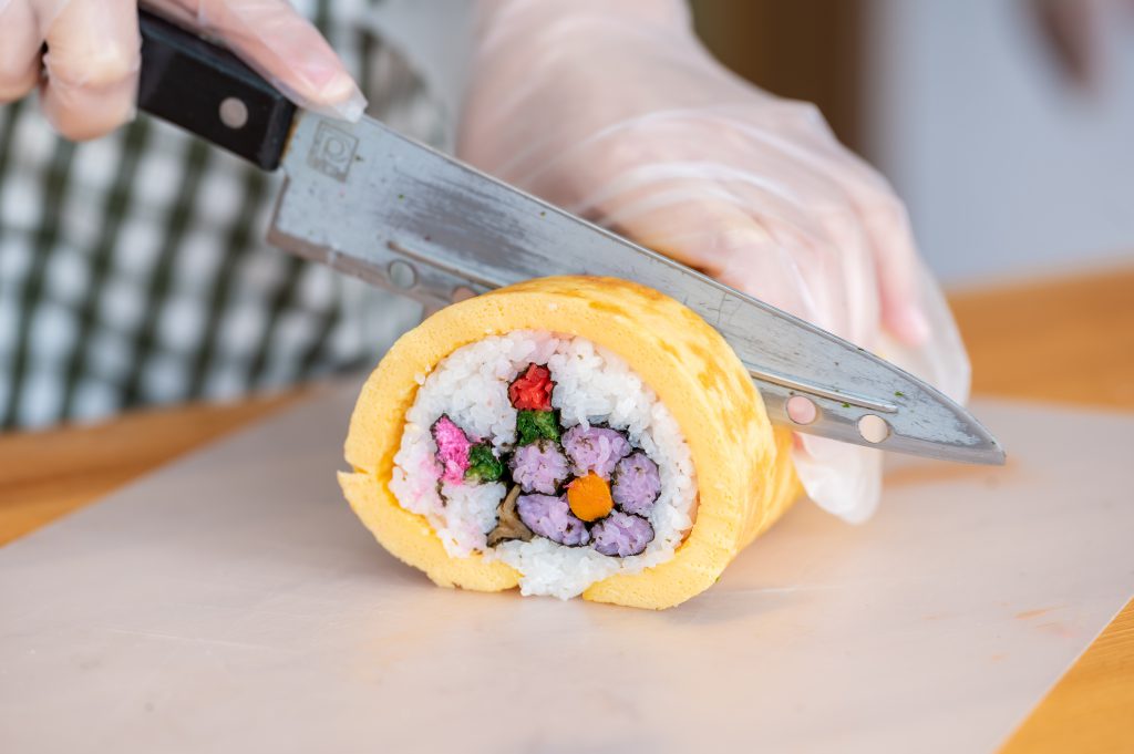 Someone cutting a big sushi roll. the ingredients inside form the shape of a flower