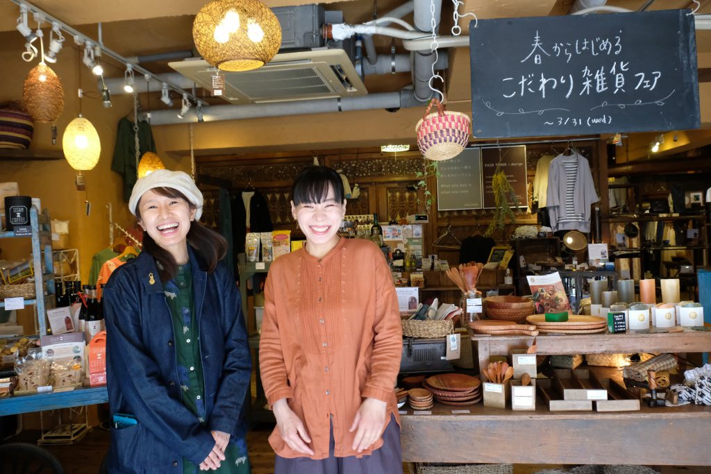 Two Japanese women are smiling in front of a shop