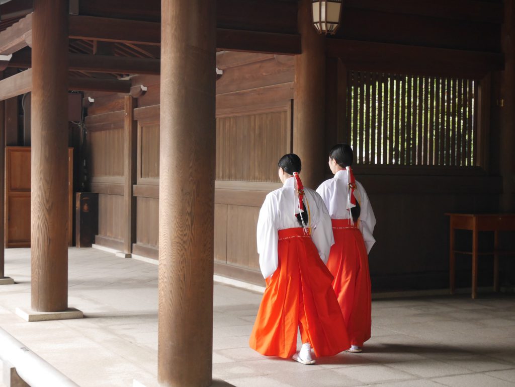 Two women in white and orange traditional dressing walk along a wooden building