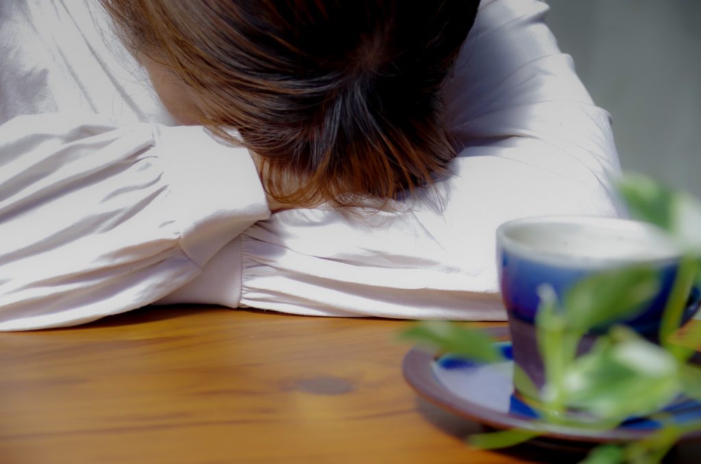 A woman is putting her head on her arms crossed on a table