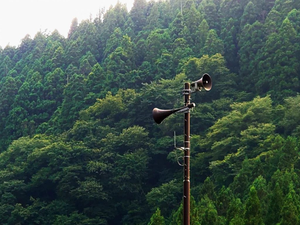 A huge pole with speakers at the top. Behind it, a forest.