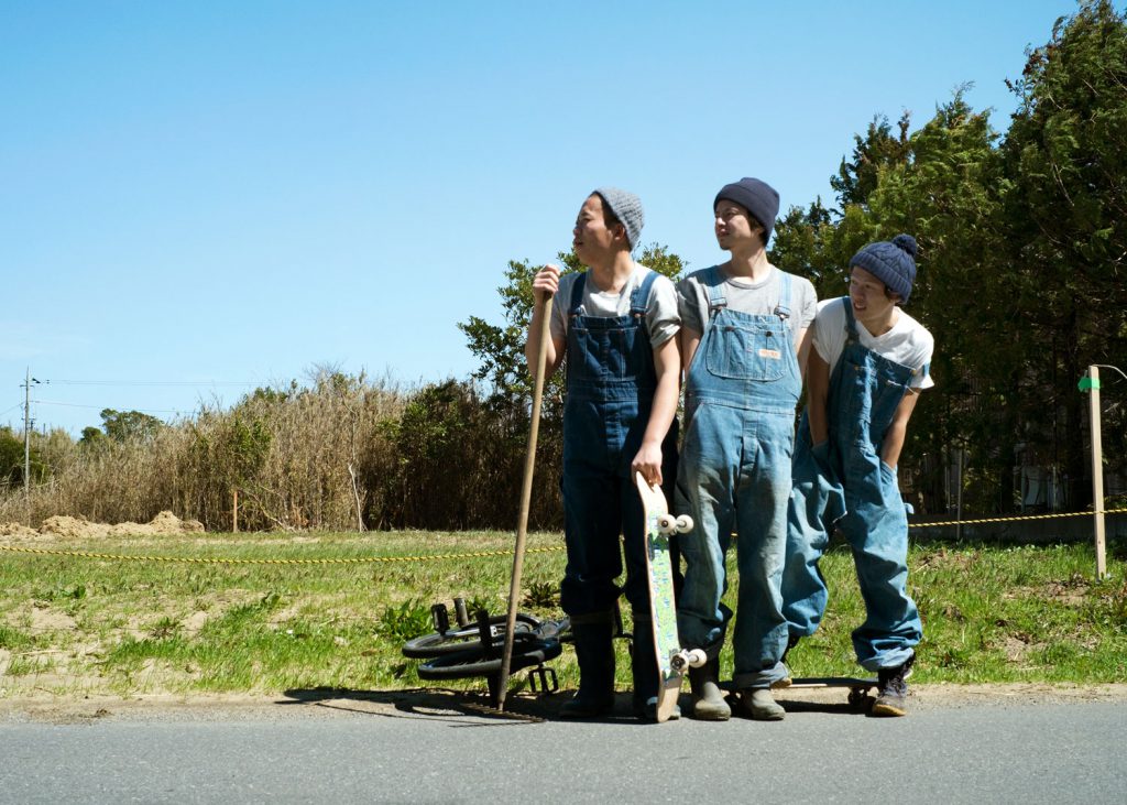 Go  with two other men. They are dressed in denim overalls and have their skateboards and BMX with them.