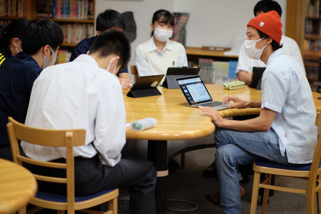 Go is sitting around a table with several high schoolers