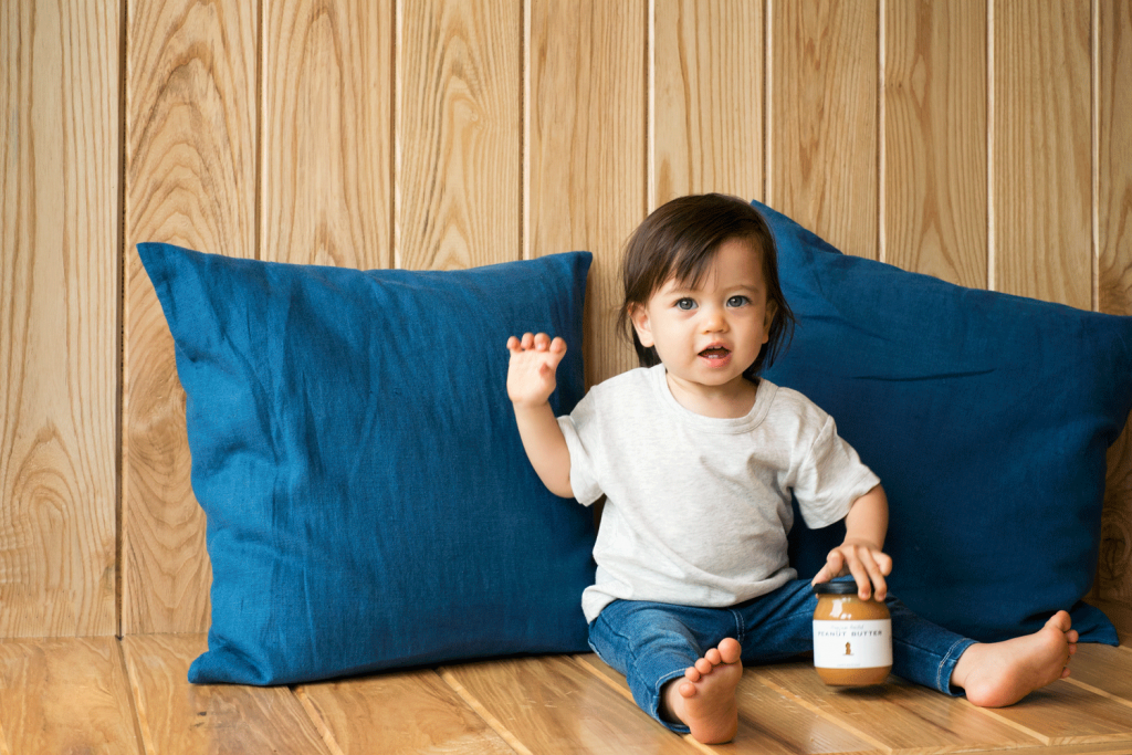 A toddler is holding a jar of Happy Nuts Day peanut butter