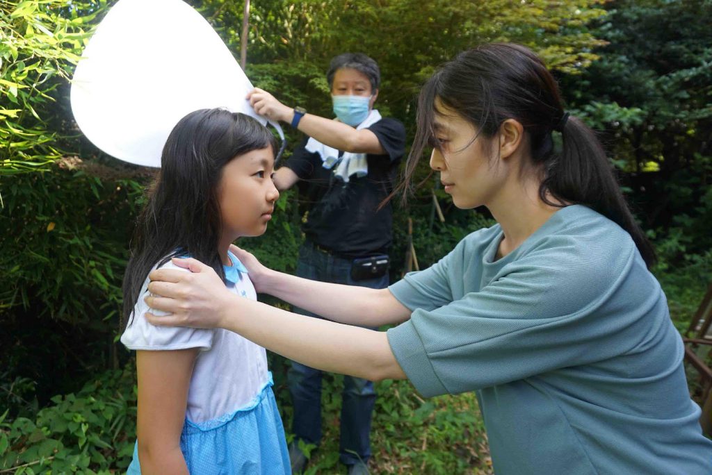 Kyoko is holding a little girl by the shoulders.