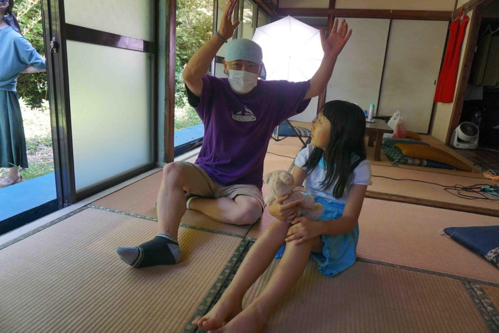 Director Hamakawa is sitting next to a little girl and explaining something doing gestures