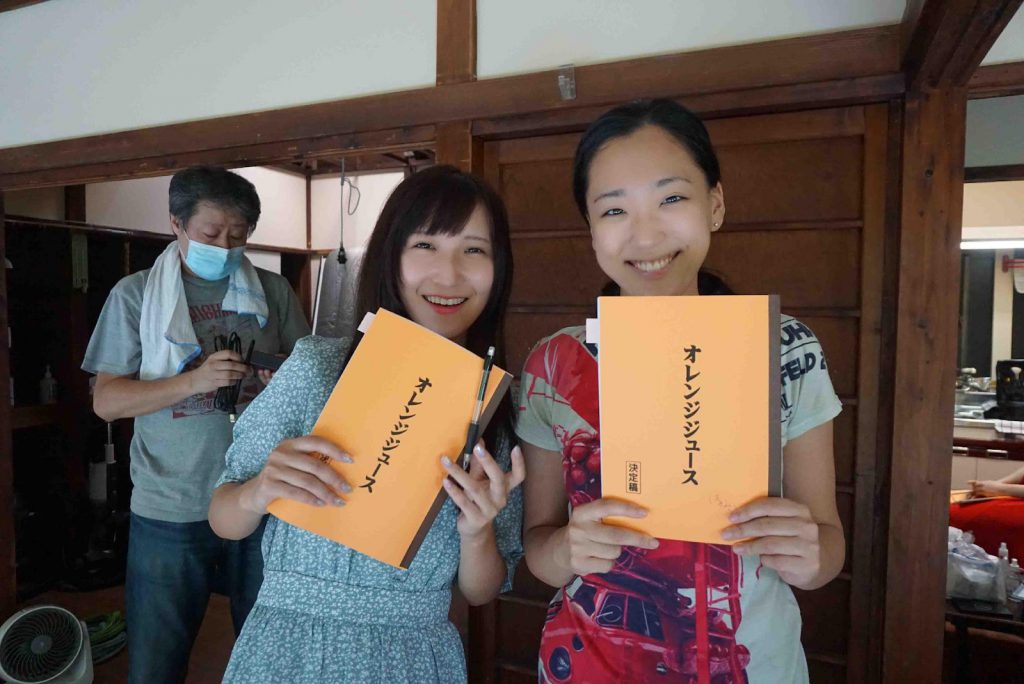 Two actresses are holding booklets and smiling to the camera