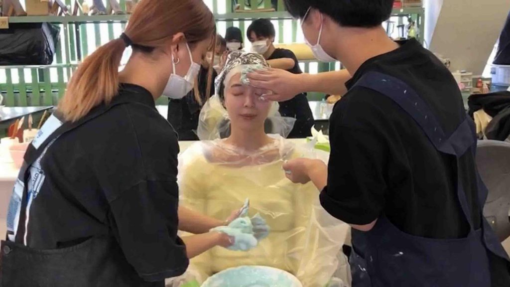 Two women are applying a paste on an actress' face