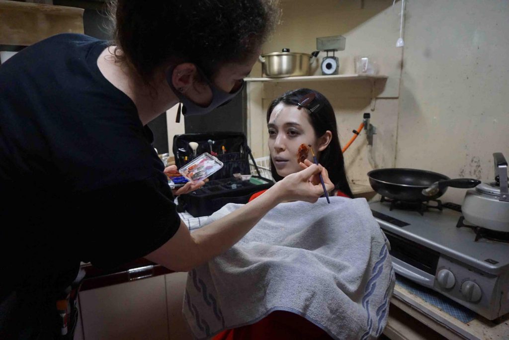 Faiza is applying bloddy-looking makeup on Kyoko's face