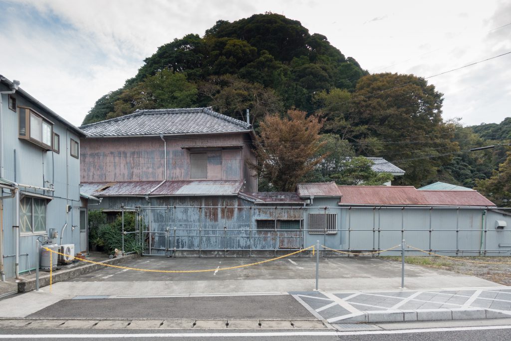 A grey abandoned building and parking lot. 