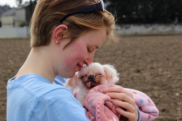 Kelsey hugging a little dog wrapped in a pink blanket