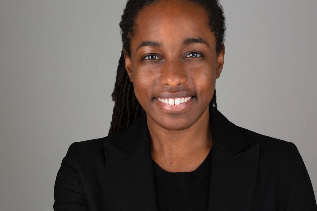 Tia Haygood, dressed in a black suit, smiles at the camera.