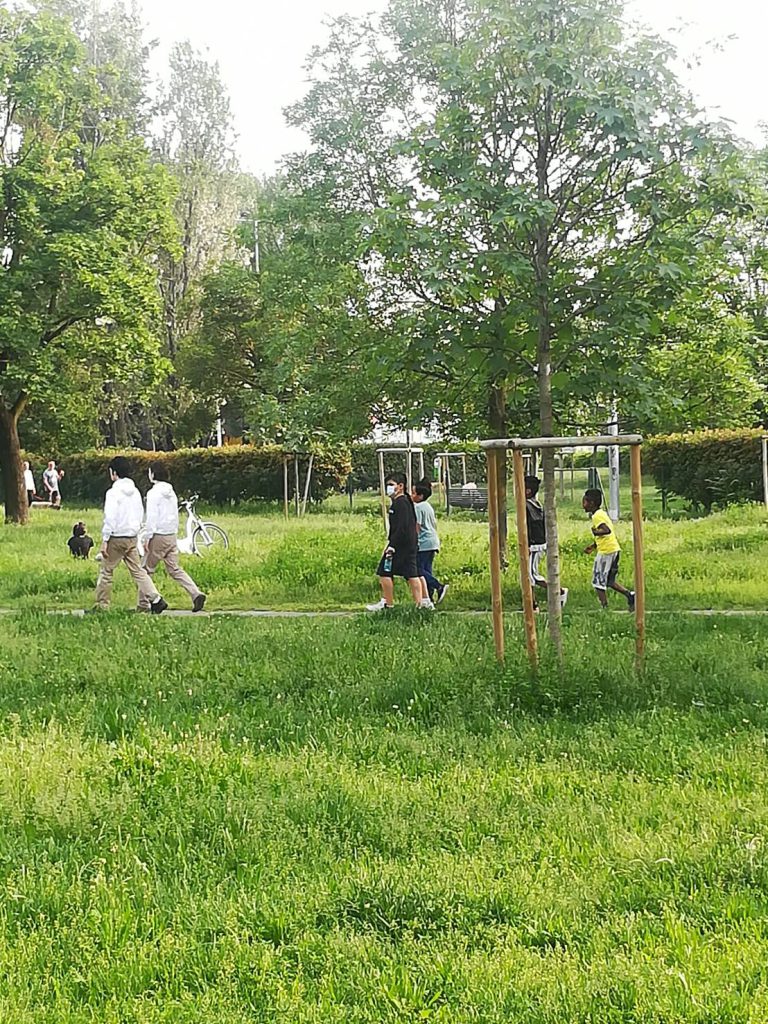 Aguyoshi, dressed in white jackets and beige trousers, walk on a path in a park. They are followed by four elementary school aged boys.