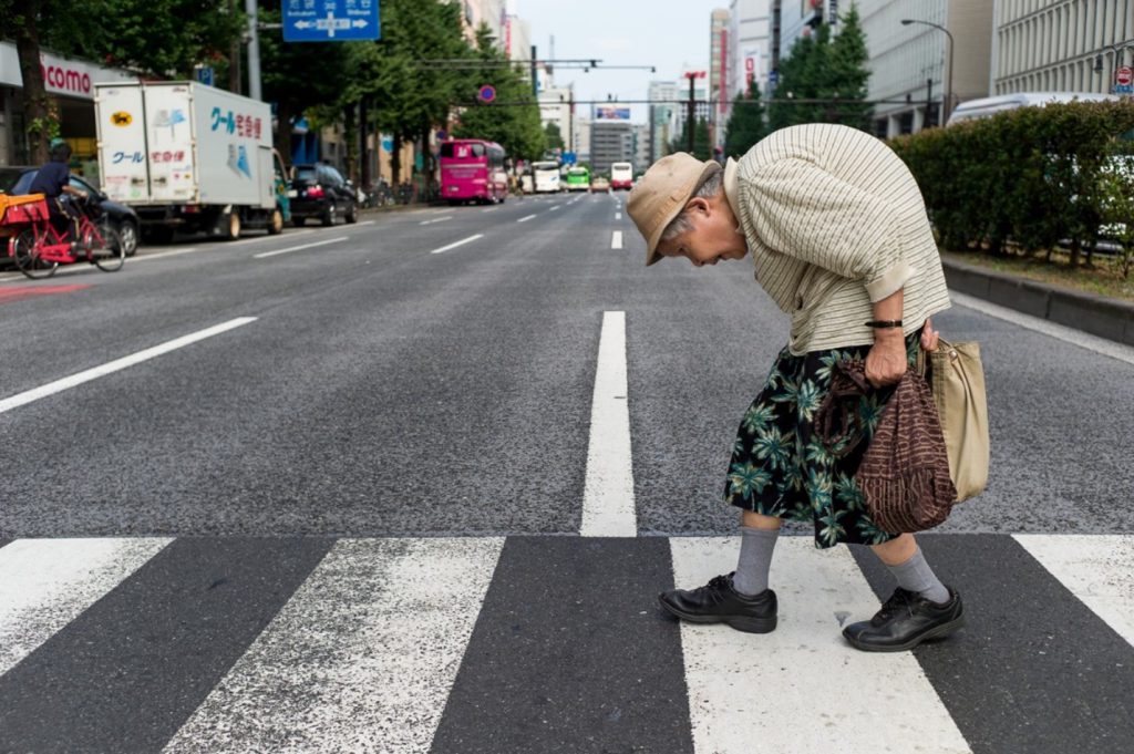 A picture taken by Lee Chapman shows an elderly woman whose back is extremely bent forward. She is crossing a zebra.