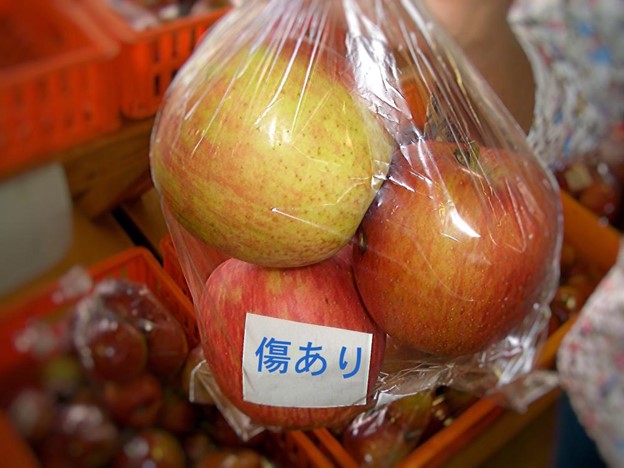 Red apples in a plastic bag on which is written kizu ari ("damaged")