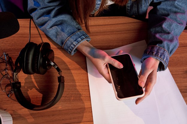 Someone is holding a smartphone above a table on which headphones are put.