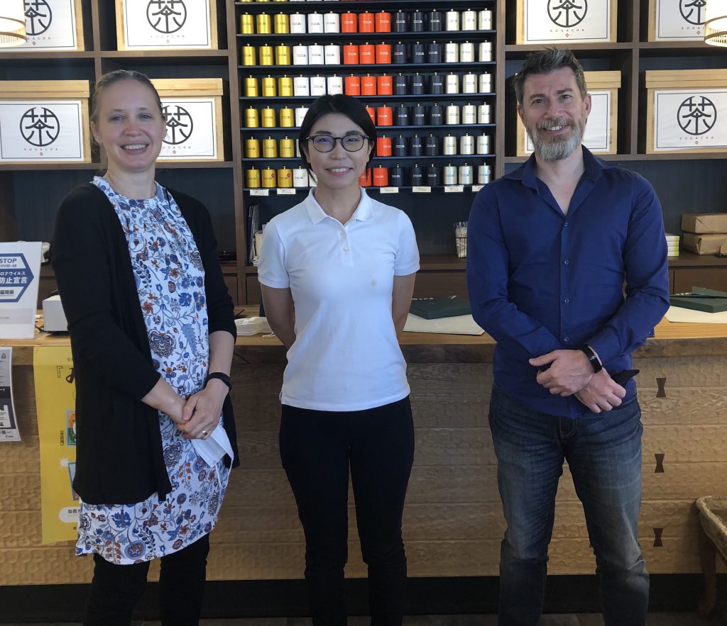 Aldo, Joelle and a young Japanese woman are standing in a shop in front of tea boxes.