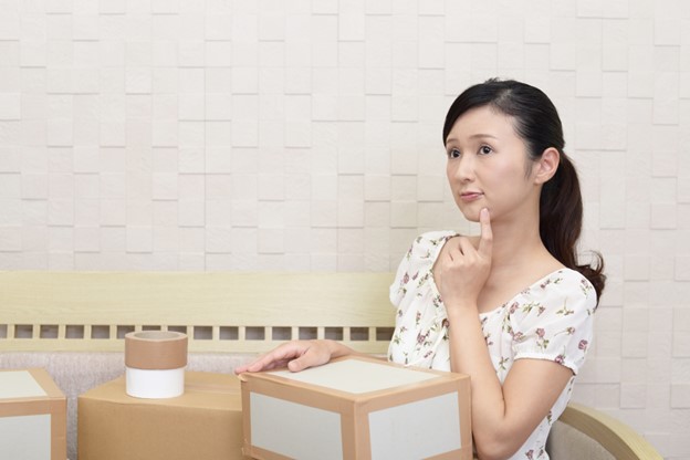 A Japanese woman is holding a carboard box that she just tapes. She seems to be pondering.