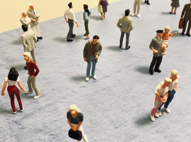 Plastic figures representing people are spread on a table. At the center, a figure seems to be standing alone.