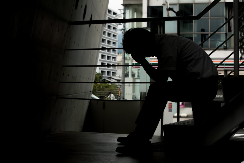 A man is sitting on stairs, his head resting on his hands in a depressed pose.