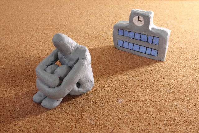 A clay figure of a person is presented sitting on the floor and turning its back to a clay figure representing a school.