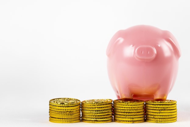 Piles of coins are stacked next to a piggy bank.