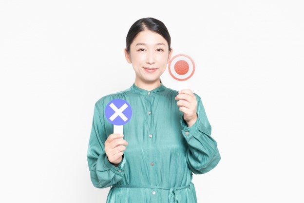A Japanese woman is holding two sings: one with a white circle on a red background, and another with a white x on a blue background