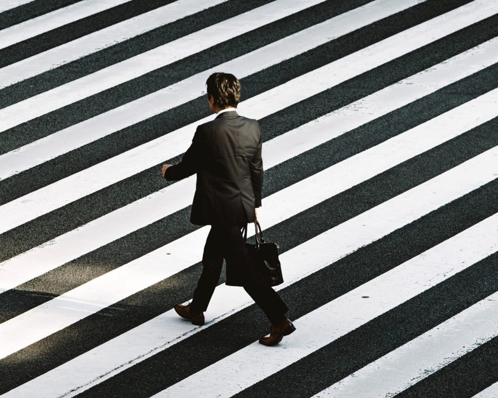 A Japanese businessman is crossing the street on a marked crosswalk