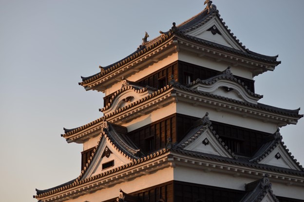 A Japanese castle with while walls and a black tile roof on the evening sky.