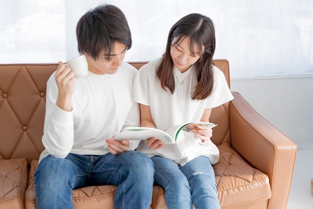 A young Japanese couple is sitting on a sofa and examining brochures.