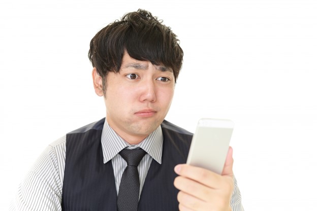 A young Japanese man is looking at his smartphone with a perplexed facial expression.