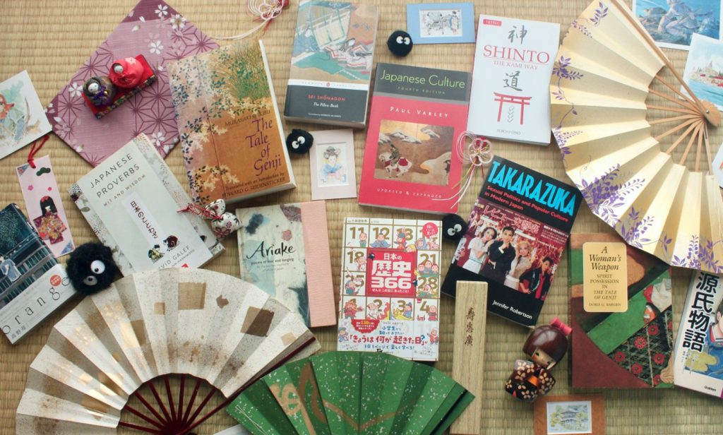 Many books about Japanese culture lay on a tatami floor, surrounded with traditional items such as paper fans.