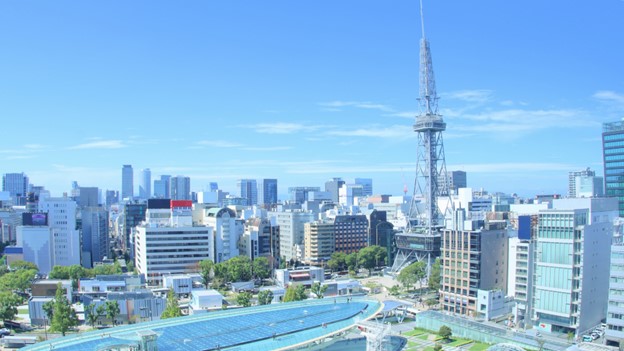 The picture seems to be taken from a 10-story building. It shows many tall buildings, but the general impression is more spacey, smaller and more open than the picture of Tokyo above. On the right of the picture, radio communication tower, which looks a bit like the Eiffel Tower, is the highest structure that detaches itself from a deep, blue sky. A the bottom of the picture, we can see small, glass buildings surrounded by trees and green.