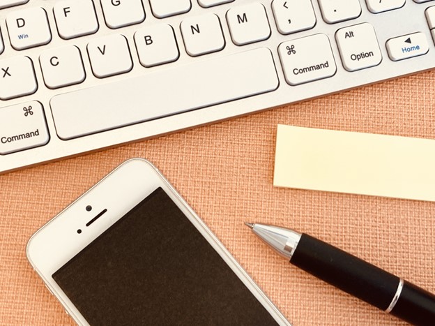 A close shot of a keyboard, a phone, a pen and sticky notes